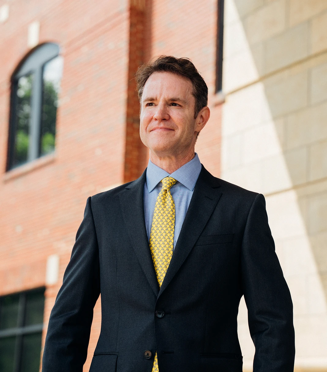 Portfolio shot of Dr. Henry Wilson outdoors, wearing a navy suit, light blue shirt and yellow tie. He looks past the camera smiling.